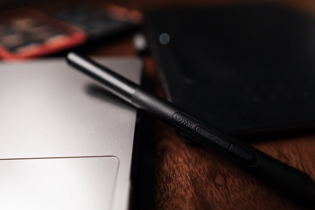 Close-up view of a stylus resting on a laptop near a digital tablet on a desk.